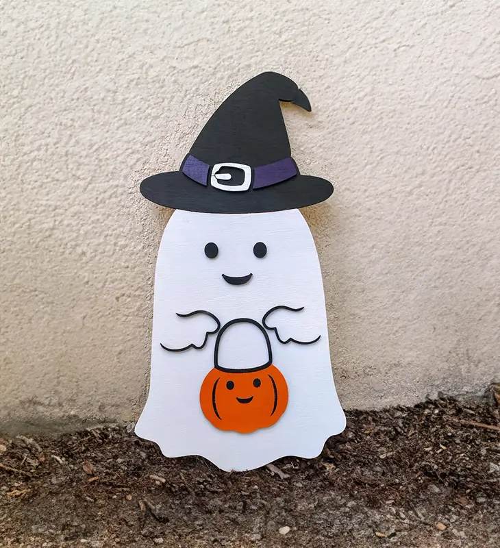 Un adorable fantasma de madera con un sombrero de bruja y una calabaza en la mano, listo para celebrar Halloween.
