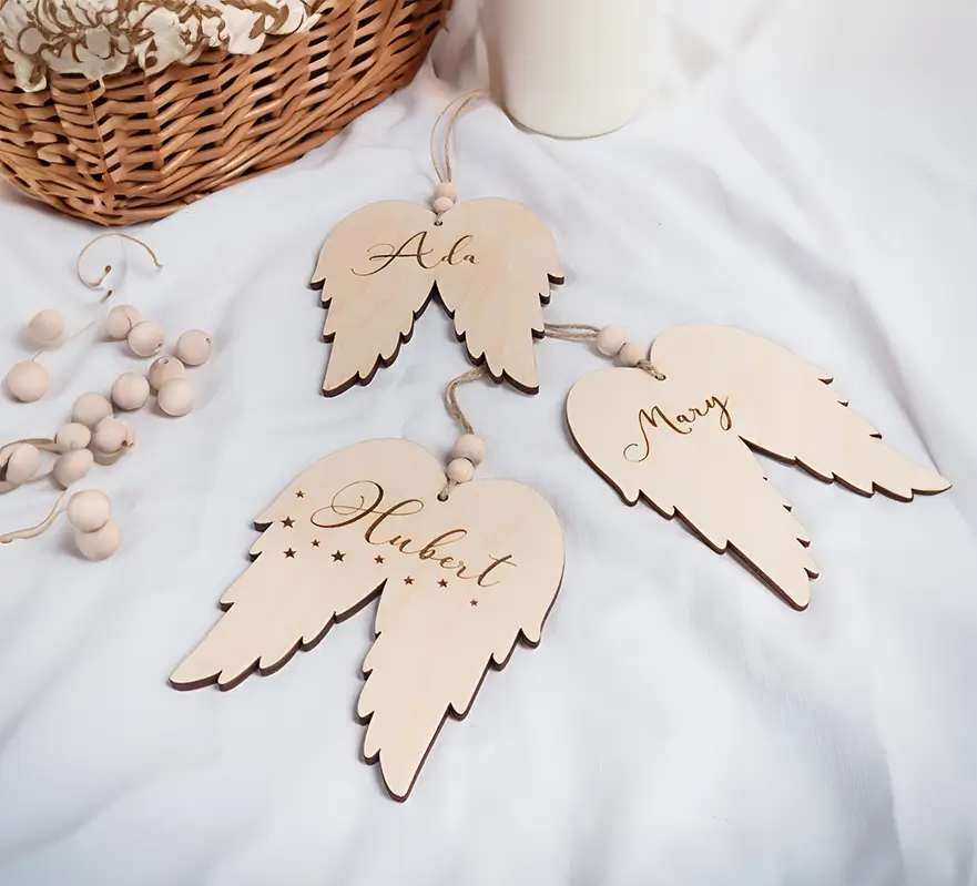 Pedazos de navideños de madera personalizados en forma de alas de ángel con los nombres "Ada", "Mary" y "Hubert".