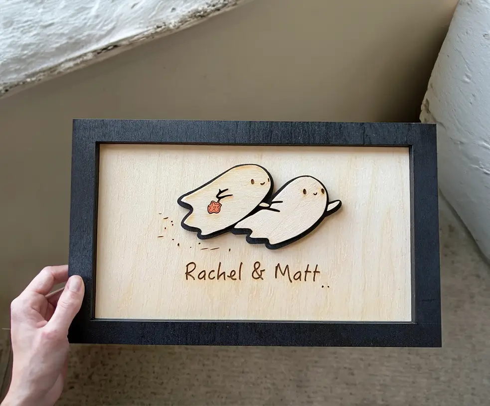 Adorno de pared de madera con diseño de dos fantasmas en 3D. Perfecto para decorar el hogar en Halloween. Incluye opción de personalización con nombres.