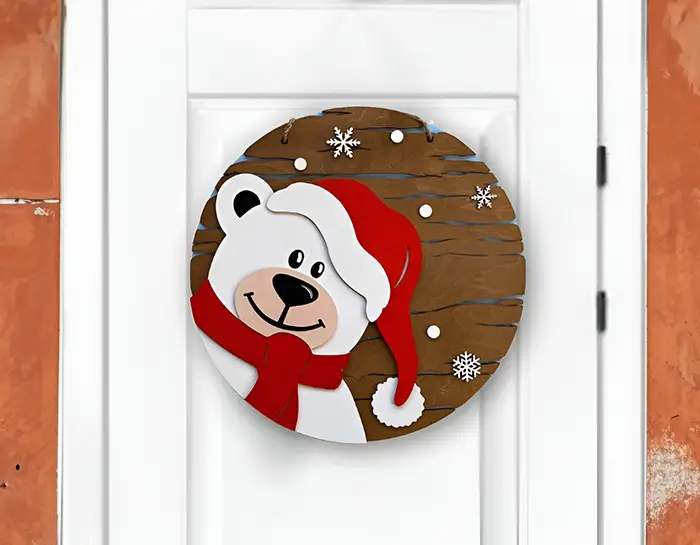 Adorno navideño de madera en forma de círculo con la cara de un oso polar sonriente. El oso lleva un gorro de Santa Claus rojo y una bufanda roja. Un fondo marrón con copos de nieve blancos crea una atmósfera invernal.