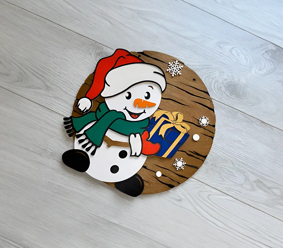 Decoración navideña artesanal: figura de muñeco de nieve de madera con un diseño alegre y festivo. El muñeco lleva un regalo y está rodeado de copos de nieve. Ideal para añadir un toque invernal a cualquier espacio.