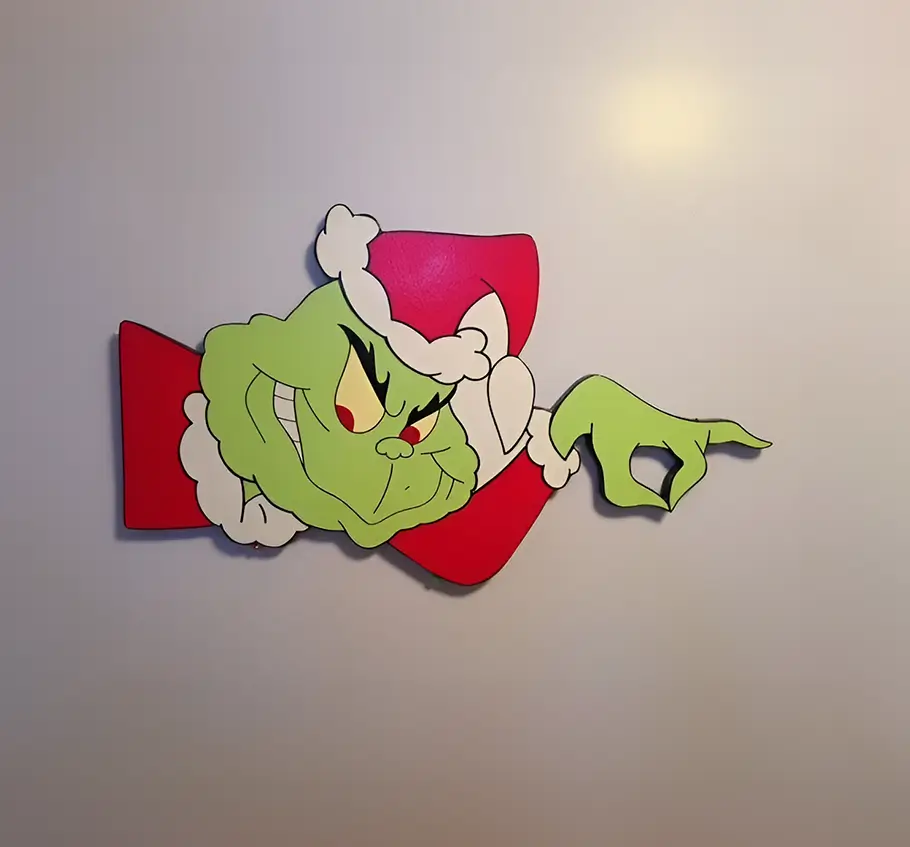 Adorno del Grinch con expresión traviesa, elaborado en materiales cortados a láser y pintado con colores vibrantes. Ideal para decoraciones festivas y ambientes navideños creativos.