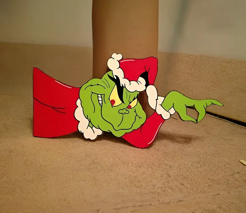 Figura decorativa navideña de madera con diseño del Grinch usando un traje rojo y gorro de Santa, colocada sobre una superficie beige para exhibición en interiores.