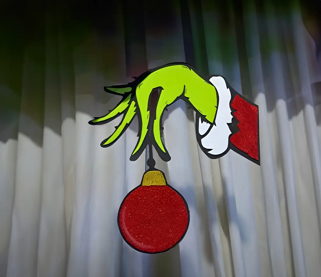Mano del Grinch como figura decorativa navideña, ideal para ambientes temáticos. Pintada con detalles realistas, colocada sobre un fondo de patrones de madera.